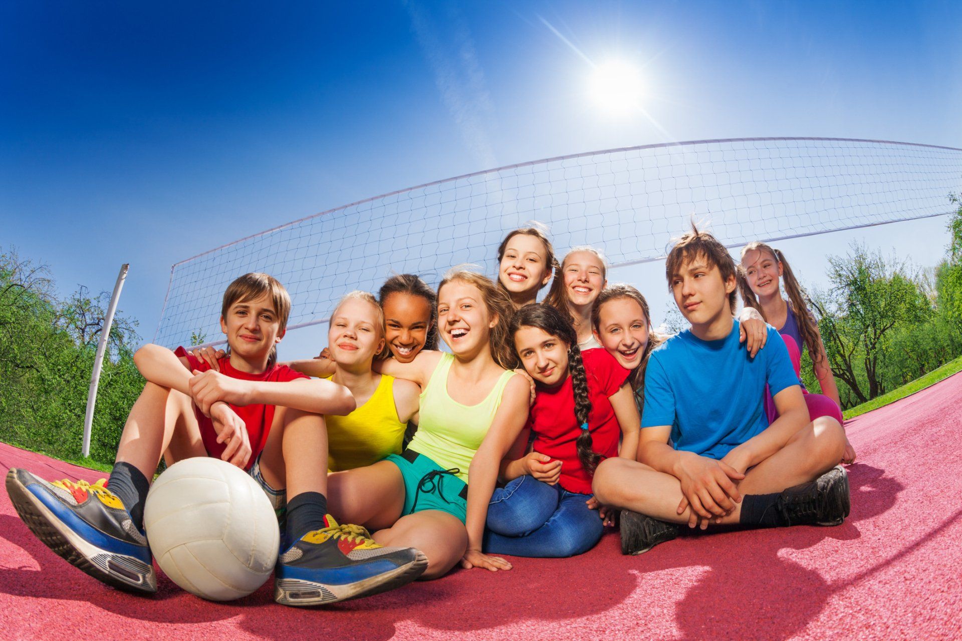 A group of young adults are sitting outside in front of a volleyball net.