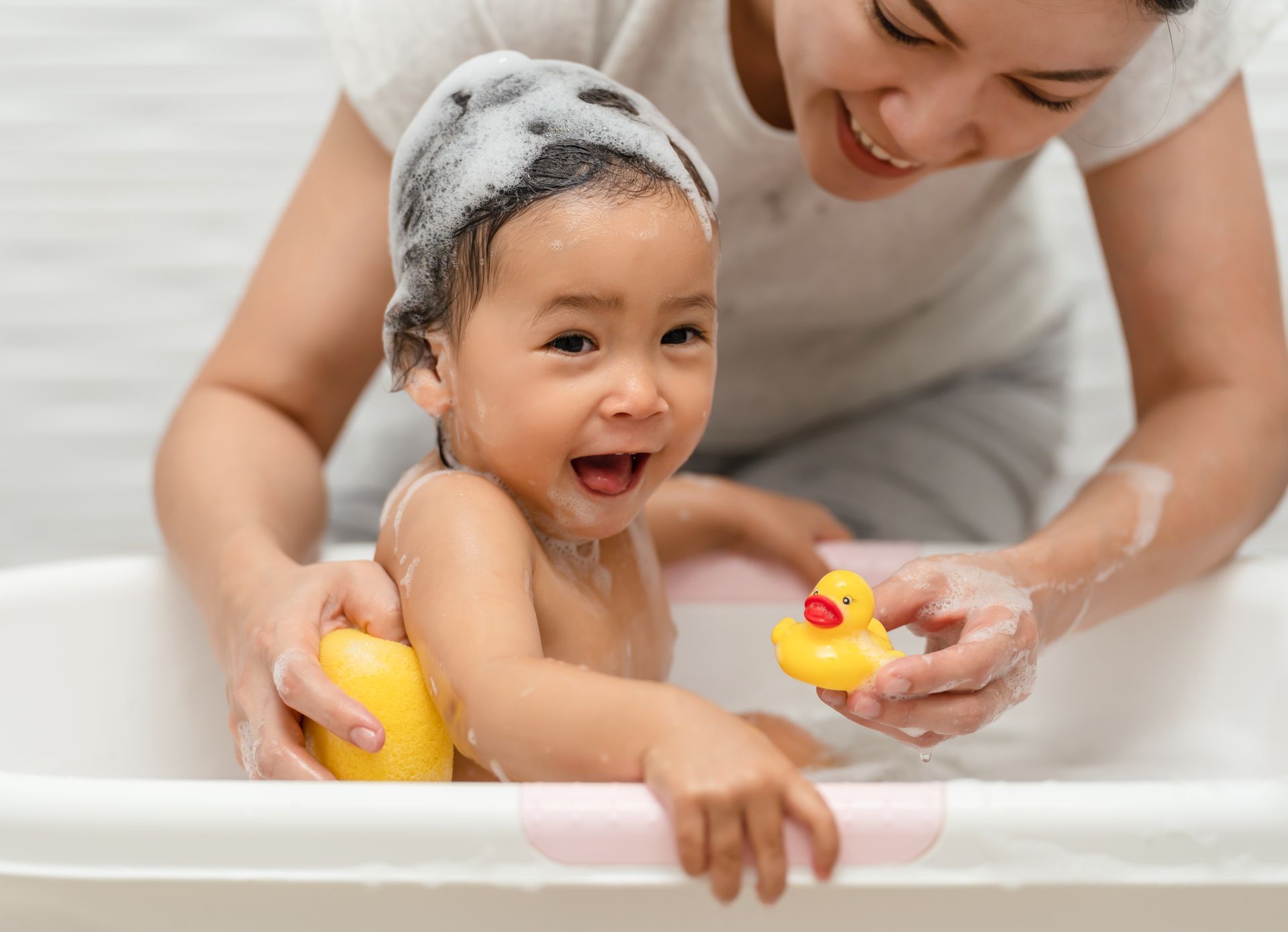 A woman is giving a baby a bath in a bathtub while holding a rubber duck.