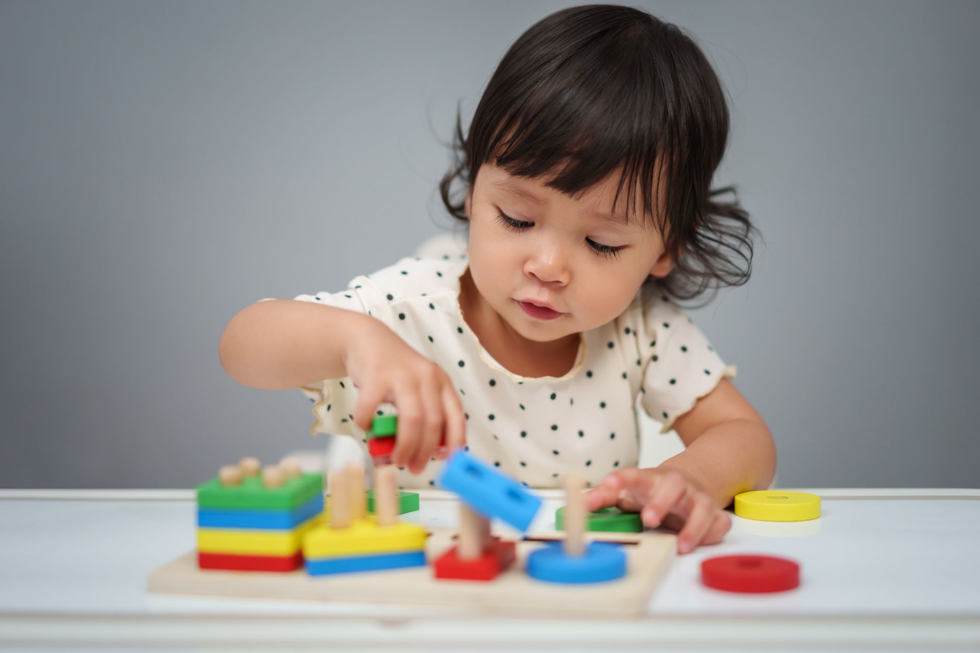 A little girl is playing with a wooden puzzle at a table.