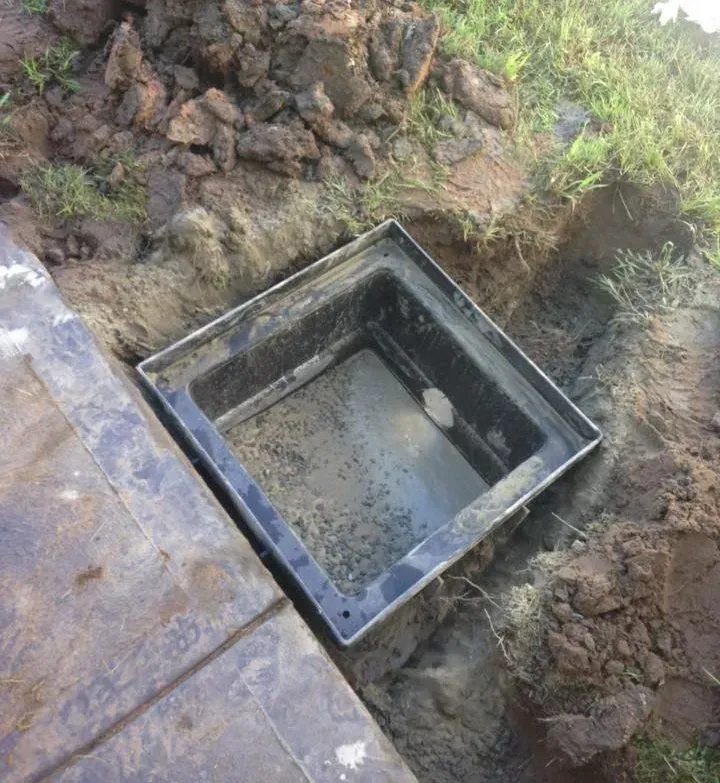 Square black tank or drain basin set in muddy ground beside a concrete slab. Square black tank or drain basin set in muddy ground beside a concrete slab.