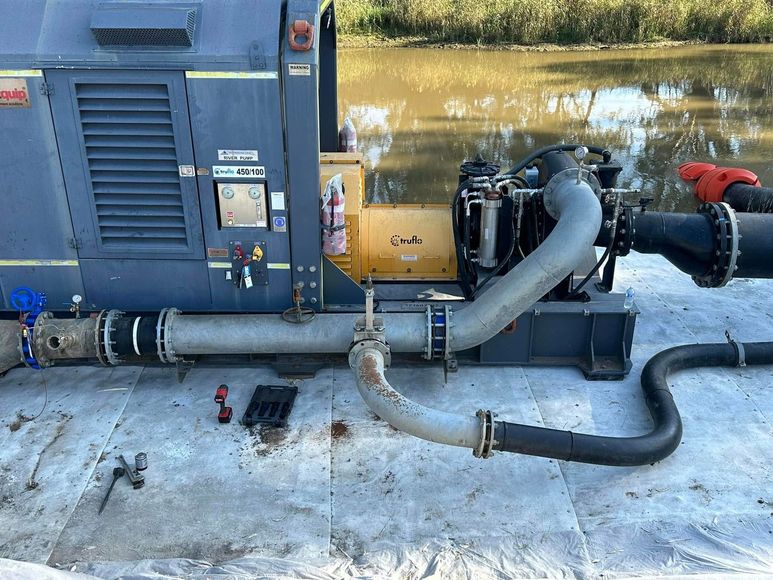 Industrial generator with black hoses and engine components on a concrete surface, partially covered in snow.