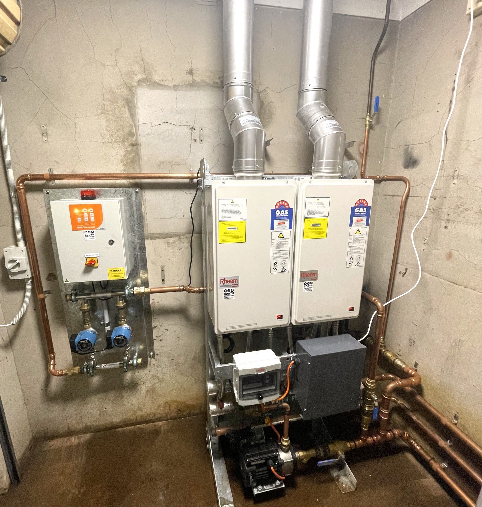 Boiler room with two wall-mounted HVAC units, ductwork, pipes, and a control panel on a concrete wall. Boiler room with two wall-mounted HVAC units, ductwork, pipes, and a control panel on a concrete wall.