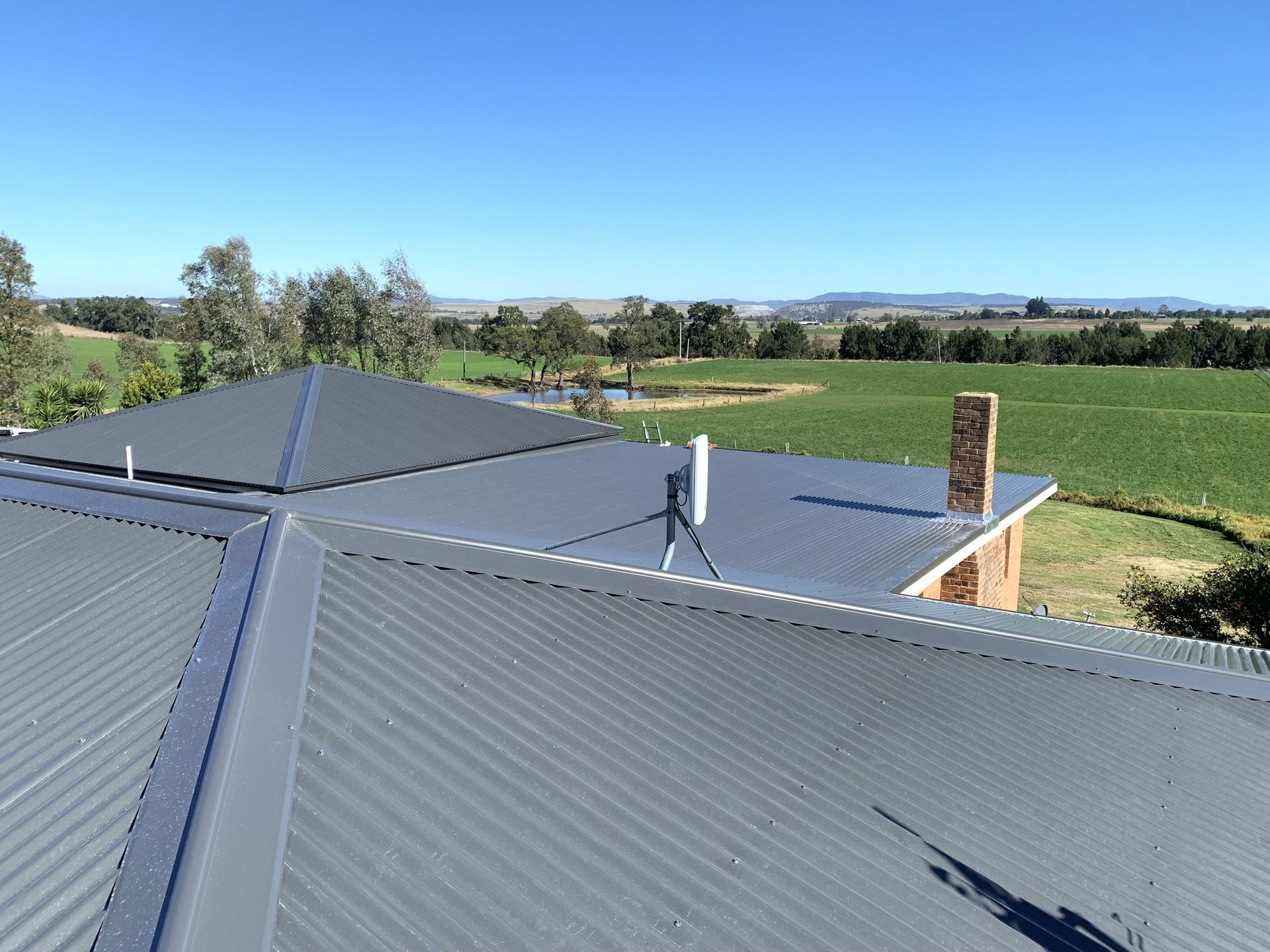 Solar roof panels with vent pipe overlooking green fields under a clear blue sky