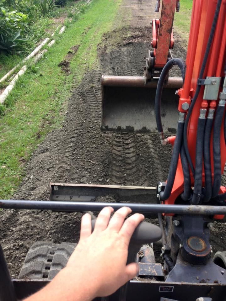 Hand on excavator controls while digging a dirt path beside a grassy embankment