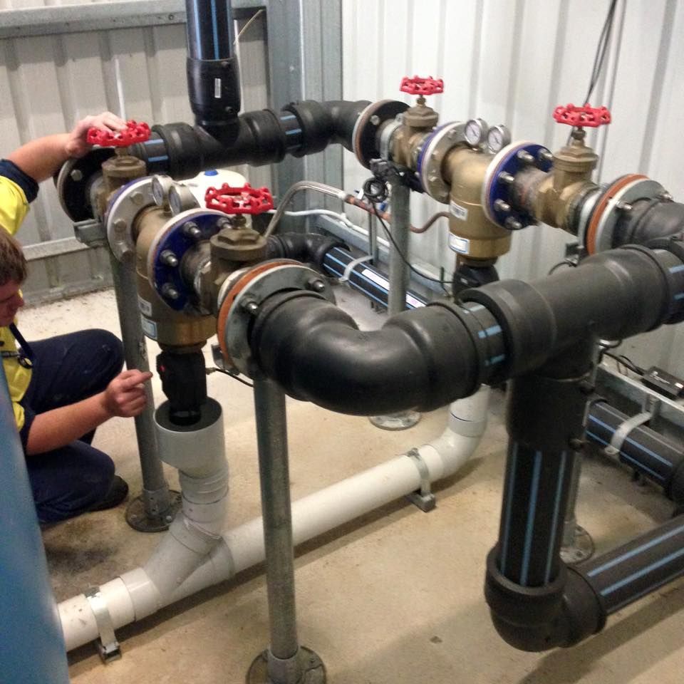 Industrial piping with black insulated pipes, red valves, and a worker inspecting the system.