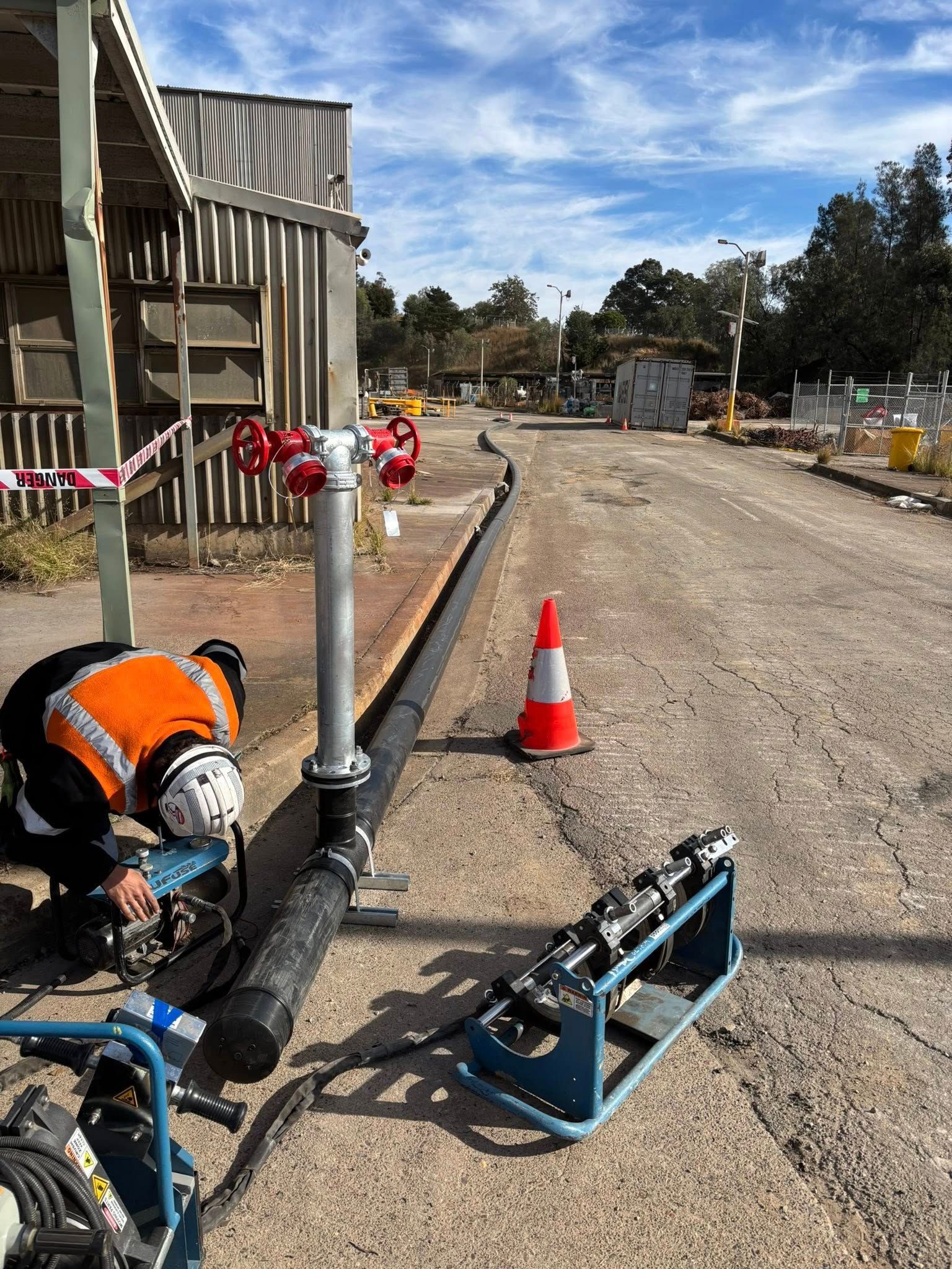 Construction site with workers, orange cones, and equipment along a gravel road by a building under repair Construction site with workers, orange cones, and equipment along a gravel road by a building under repair