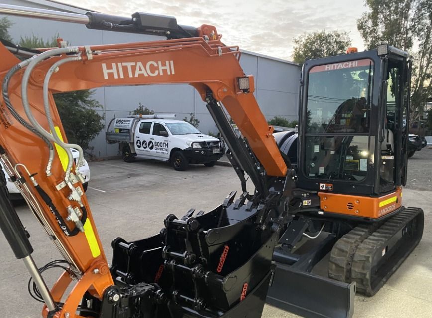 Orange Hitachi excavator parked in a lot, with a white pickup truck in the background. Orange Hitachi excavator parked in a lot, with a white pickup truck in the background.