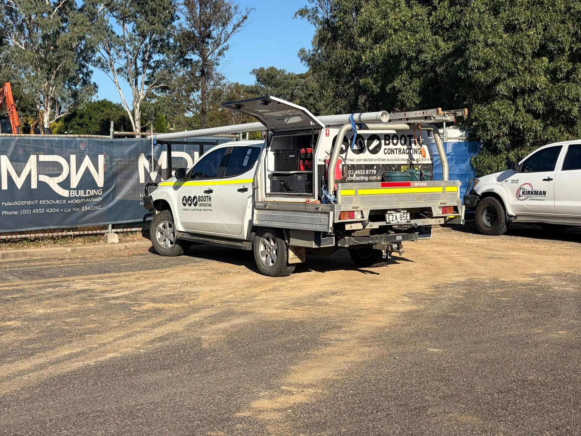 White utility truck with open rear parked on a dirt lot beside a fence and other vehicles