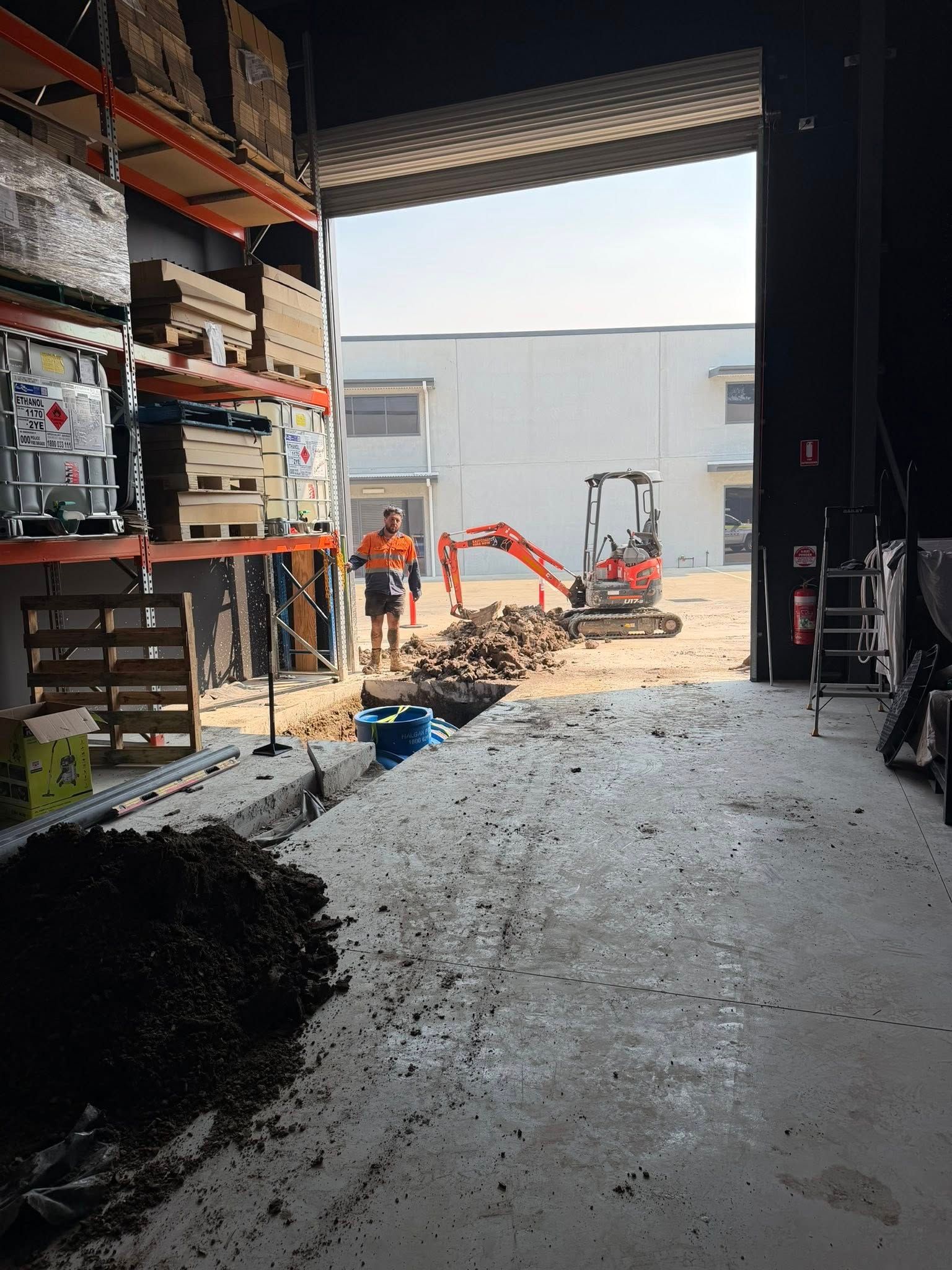 Construction workers and orange excavator inside a warehouse doorway, with gravel piled on the floor. Construction workers and orange excavator inside a warehouse doorway, with gravel piled on the floor.