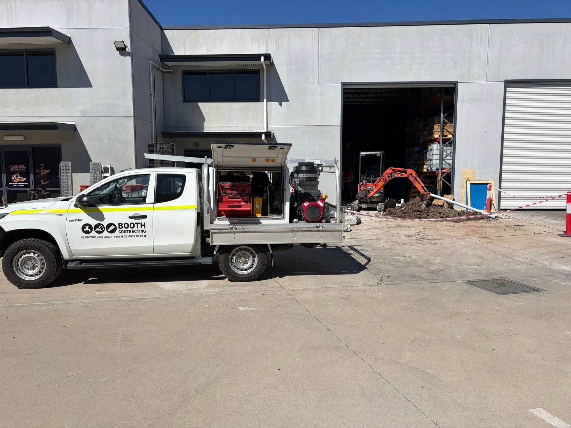 White service truck parked outside industrial bays with construction equipment inside a warehouse. White service truck parked outside industrial bays with construction equipment inside a warehouse.