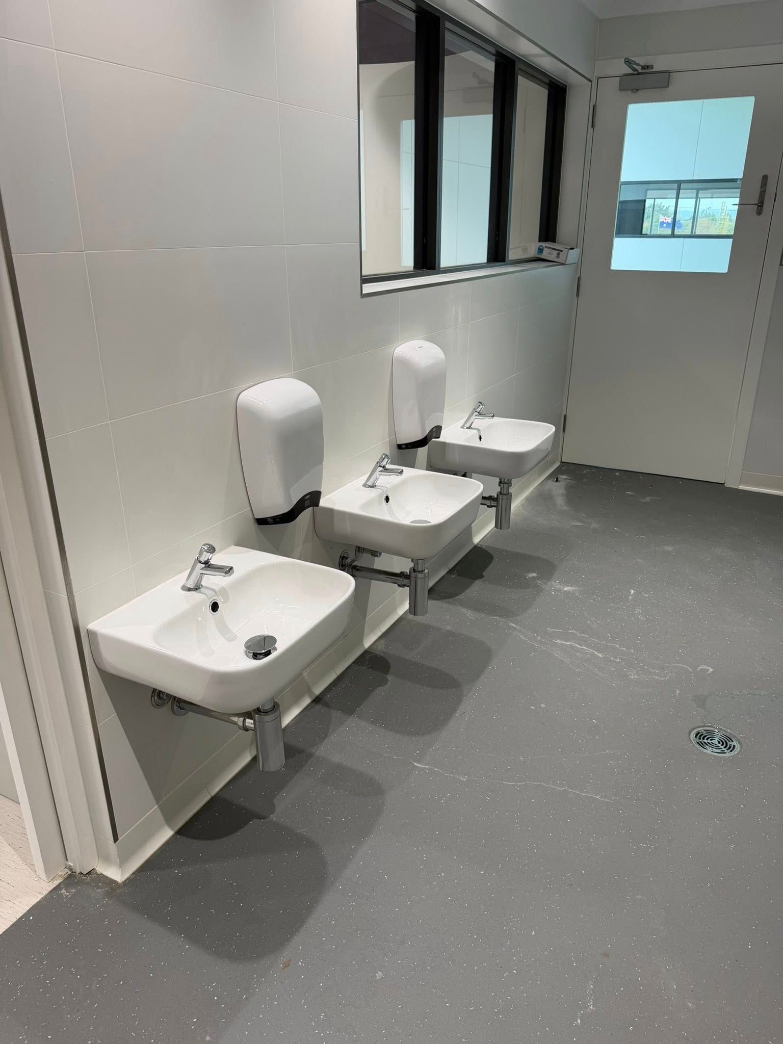 Public restroom with three wall-mounted sinks, mirrors, and gray flooring. Public restroom with three wall-mounted sinks, mirrors, and gray flooring.