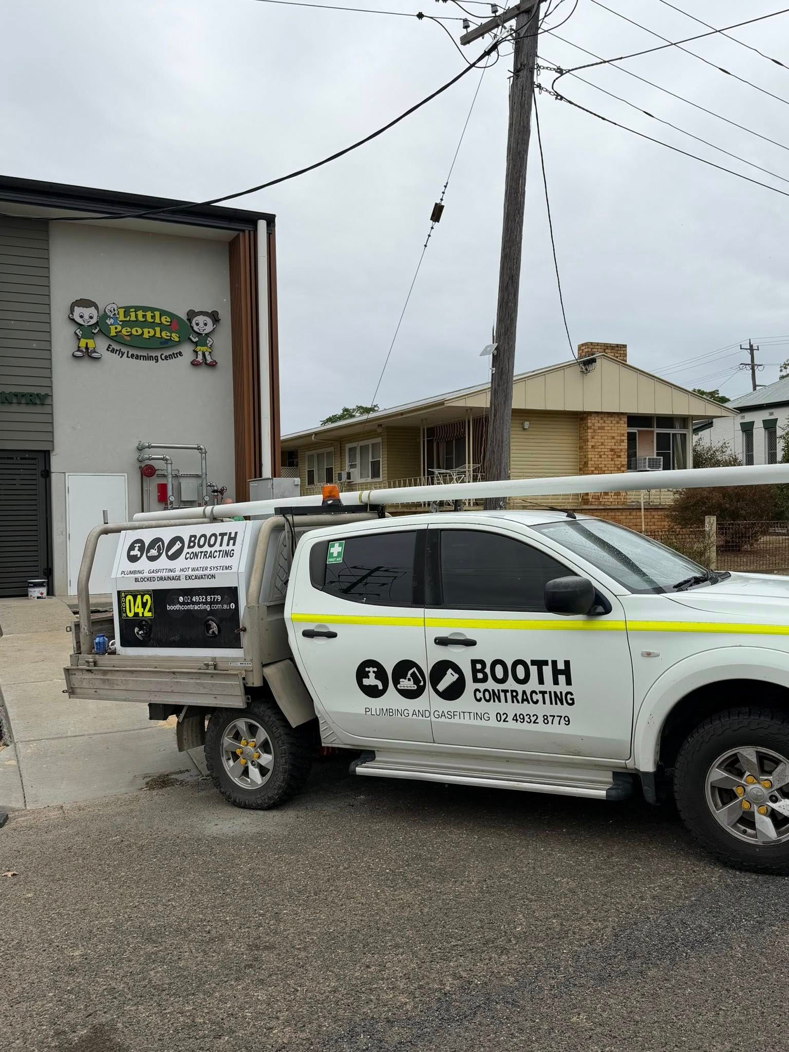 White BOOTH Services truck parked beside a utility pole and building in a gravel lot under cloudy skies