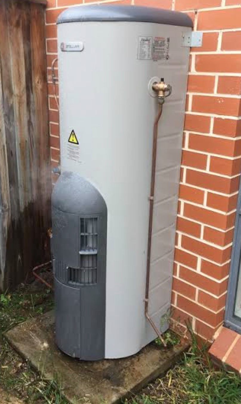 Gray outdoor hot water heater tank beside a brick wall and wooden fence. Gray outdoor hot water heater tank beside a brick wall and wooden fence.