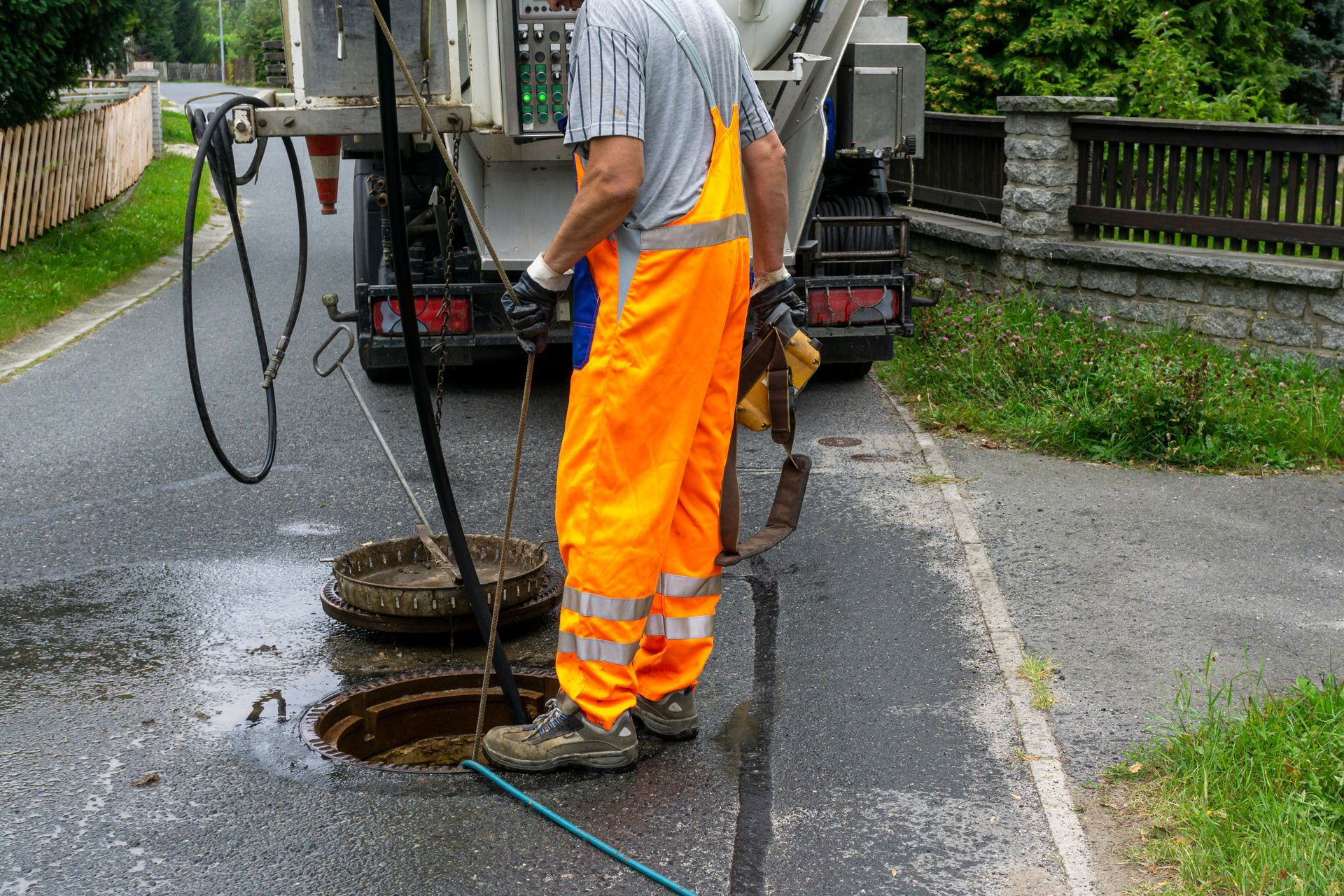 Worker in orange safety pants cleaning a manhole on a wet road with a vacuum hose Worker in orange safety pants cleaning a manhole on a wet road with a vacuum hose