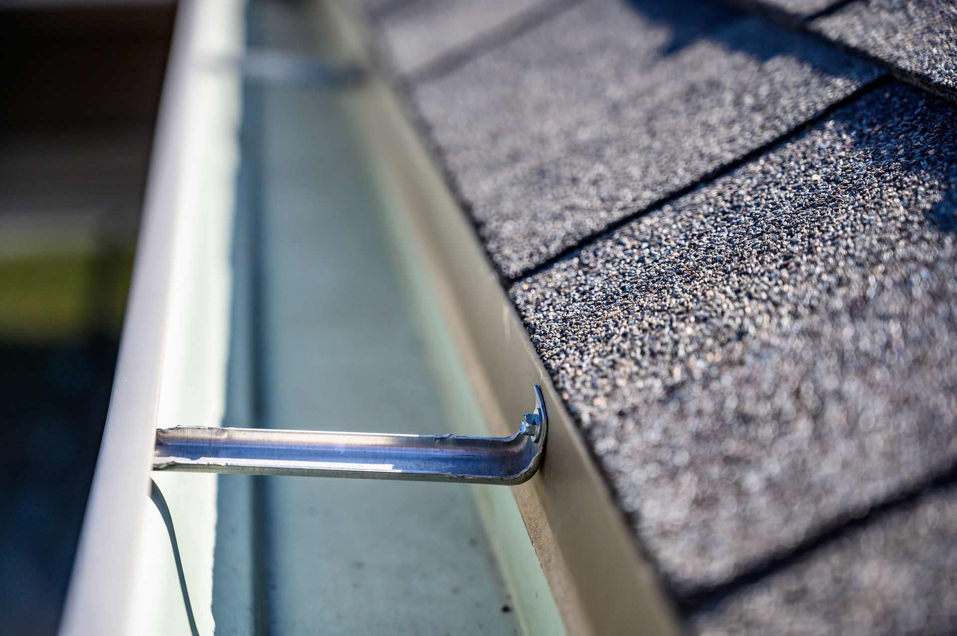 Gutter cleaning tool on a roof edge beside gray asphalt shingles