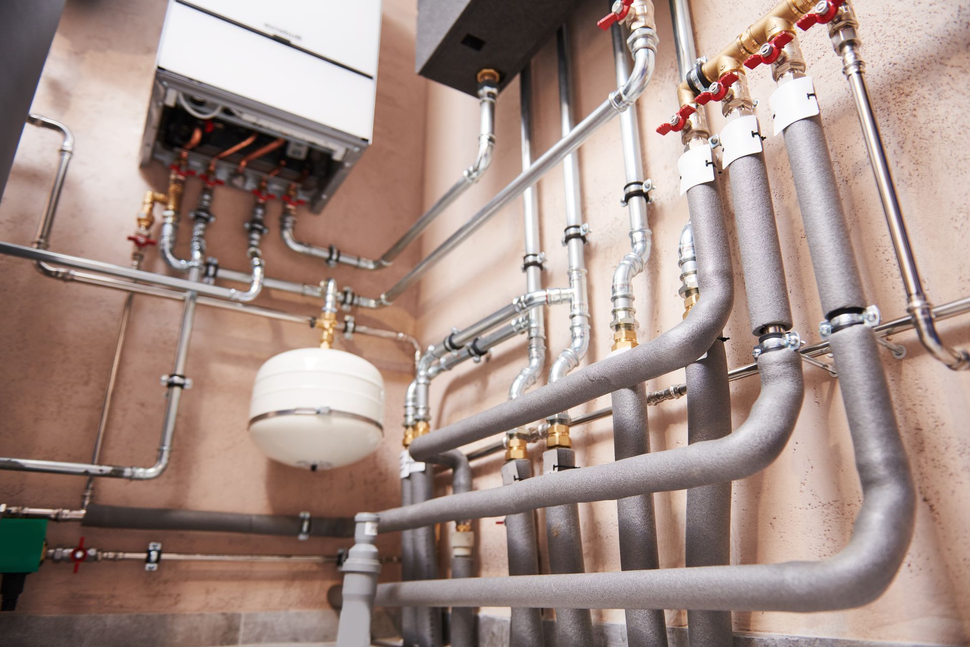 Industrial piping and tanks in a utility room with exposed metal pipes along the wall Industrial piping and tanks in a utility room with exposed metal pipes along the wall