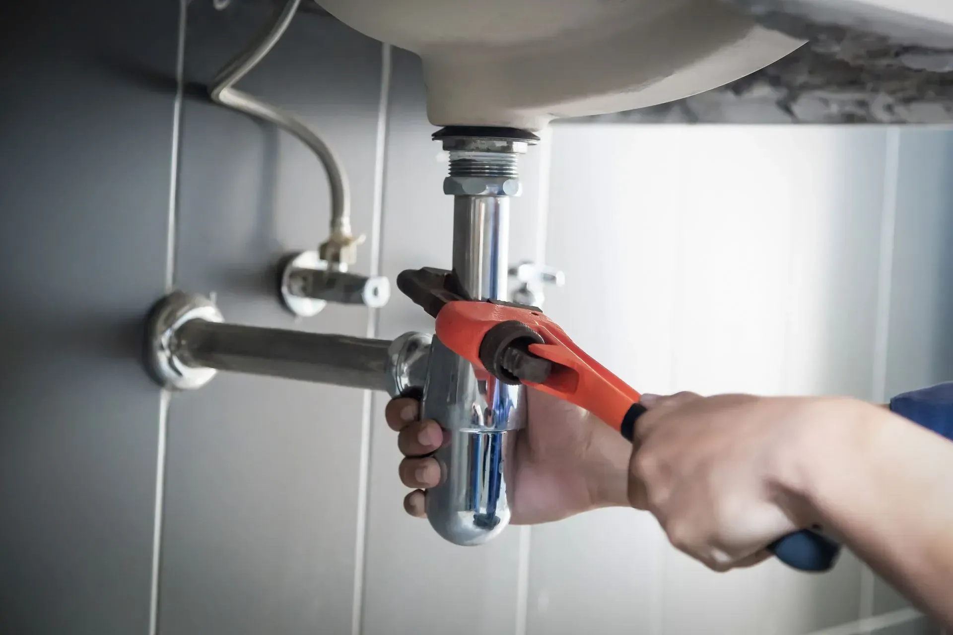 Hands using red pipe wrench to tighten a sink drain under a bathroom sink Hands using red pipe wrench to tighten a sink drain under a bathroom sink
