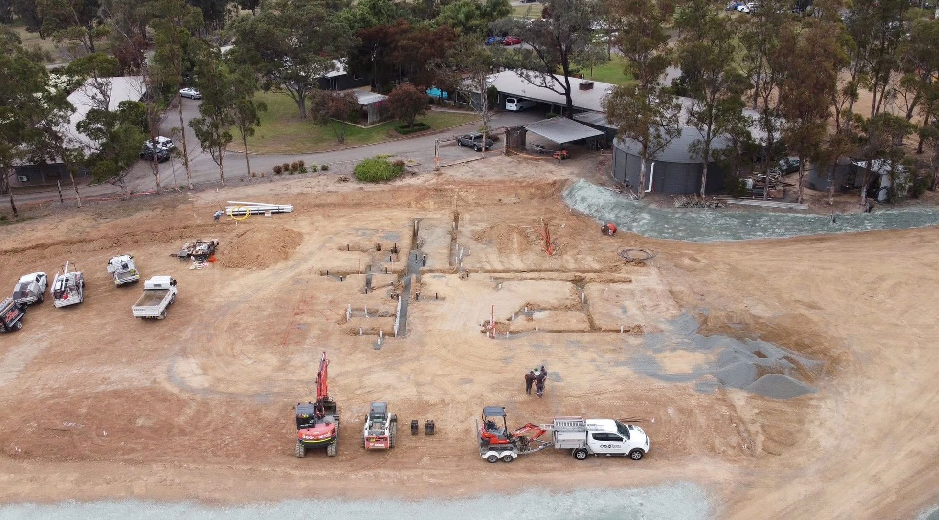 Aerial view of an excavated construction site with machinery, dirt paths, and trees along the edge