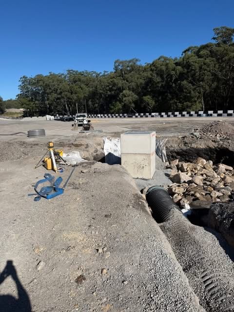 Road construction site with concrete culvert, excavator, and rubble beside a roadside drainage ditch