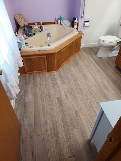 A bathroom with light wood-look flooring, a corner jetted tub with wooden paneling, purple walls, and a white toilet.