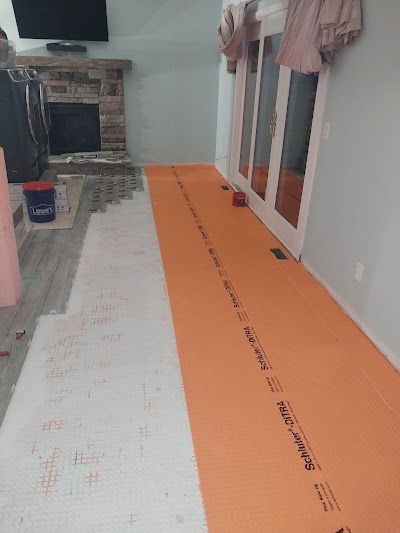 A room floor undergoing renovation with a strip of orange Schluter-DITRA underlayment next to a section of white subfloor.