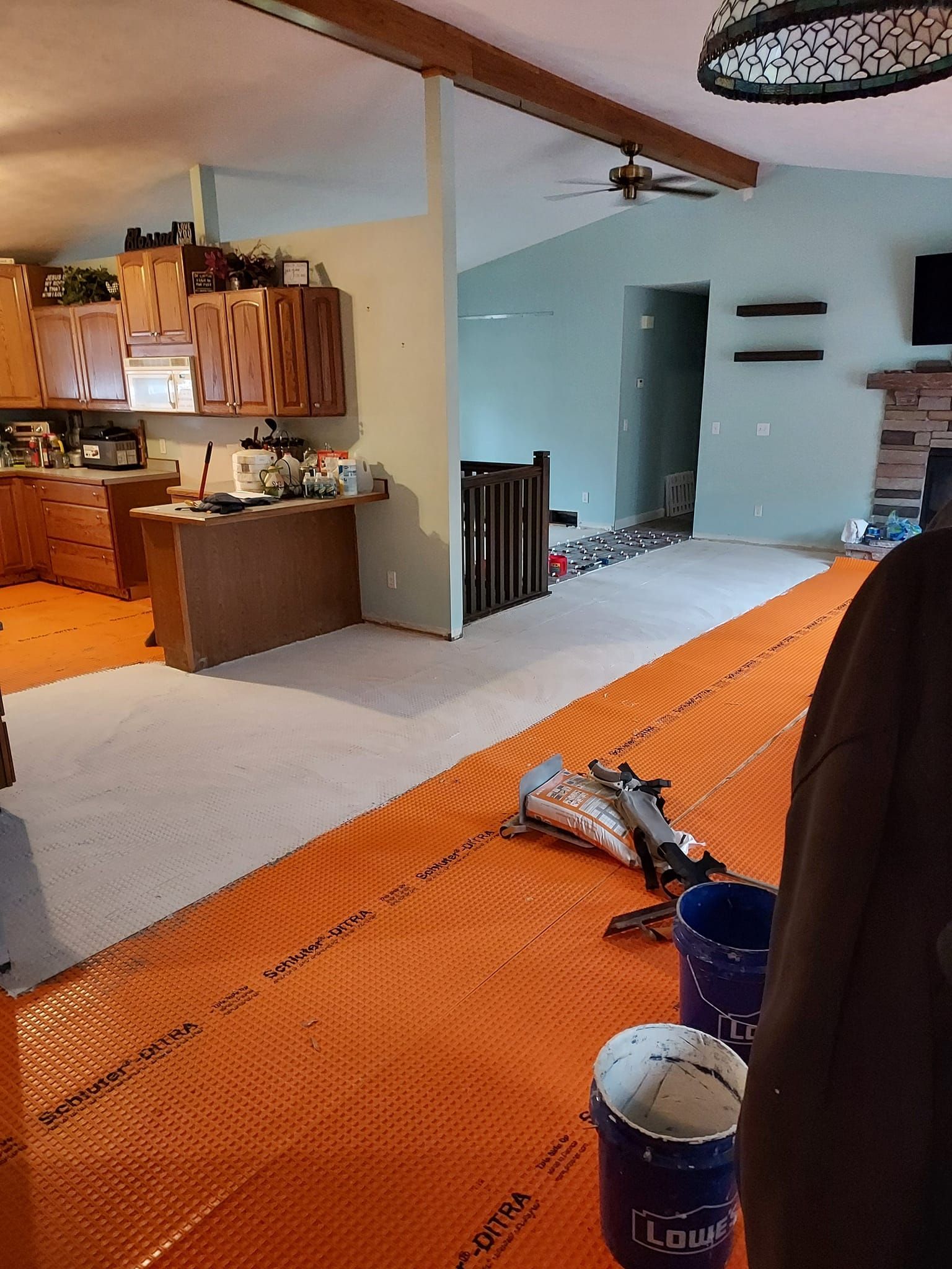 An orange underlayment membrane is installed on a floor, with buckets and construction tools nearby in a room.