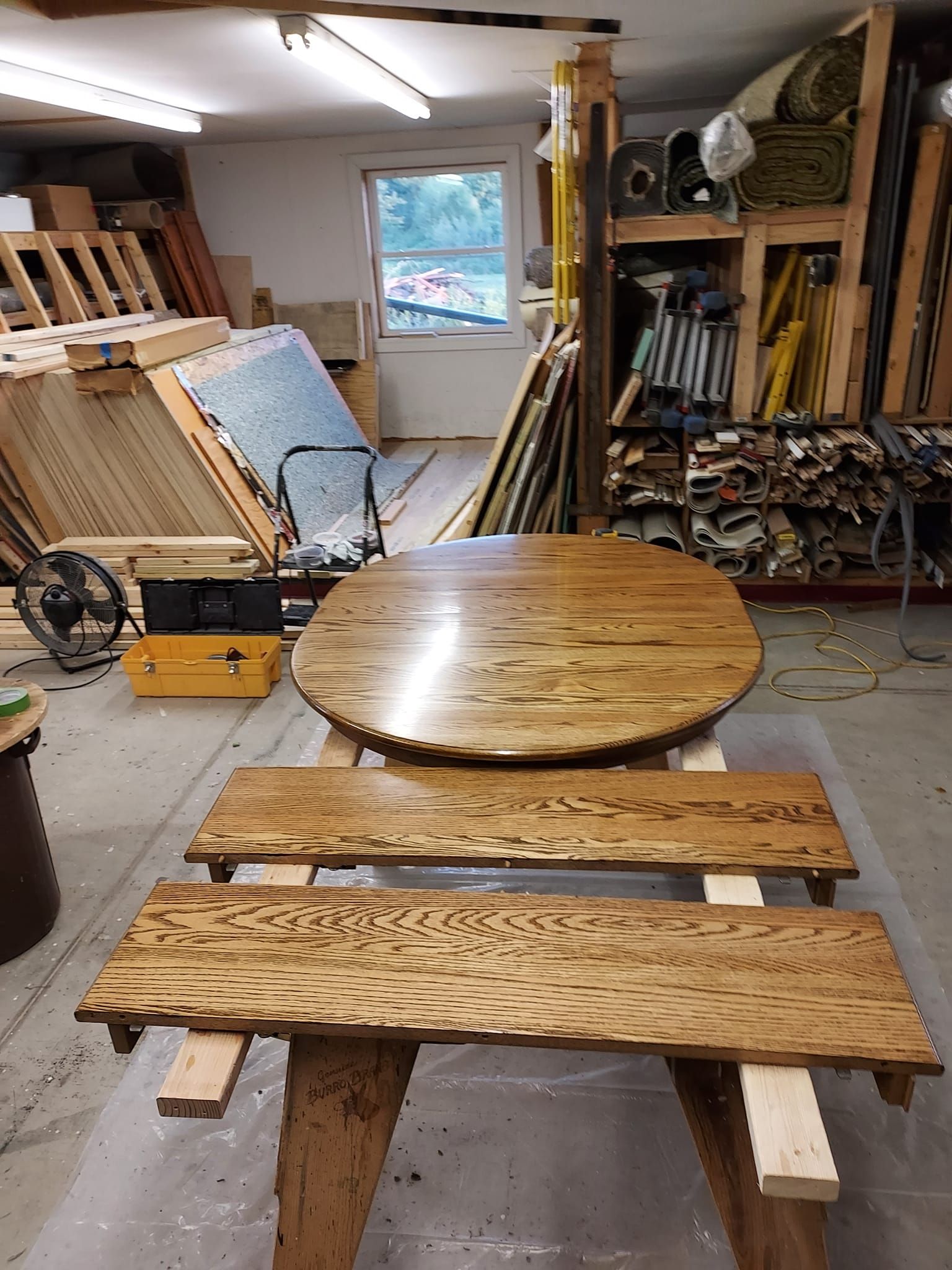 A round wooden tabletop and two matching rectangular wooden benches laid out on a workshop floor.