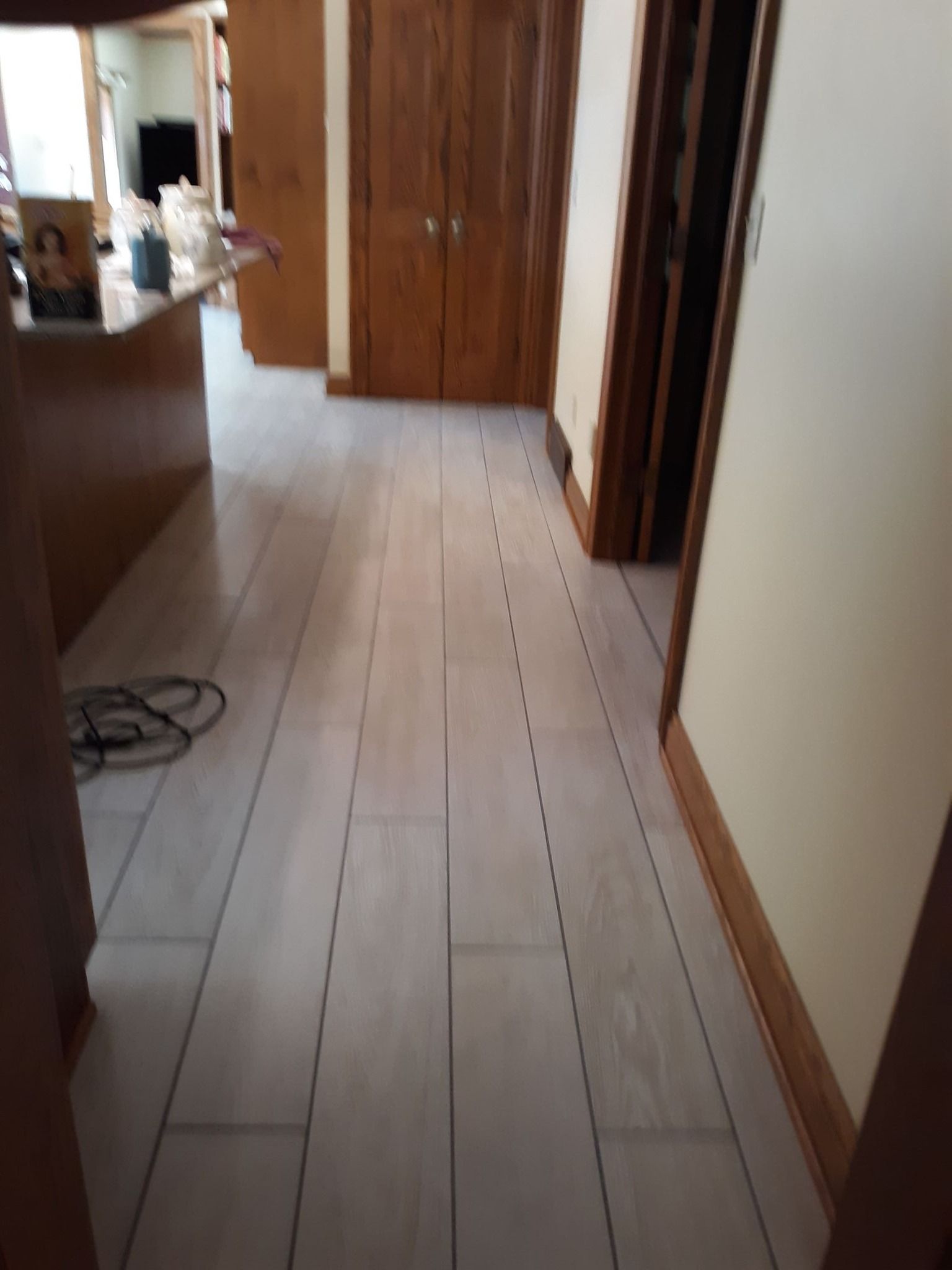 A hallway with light-colored plank flooring leading toward wooden doors, with a line of digital marks on the floor.