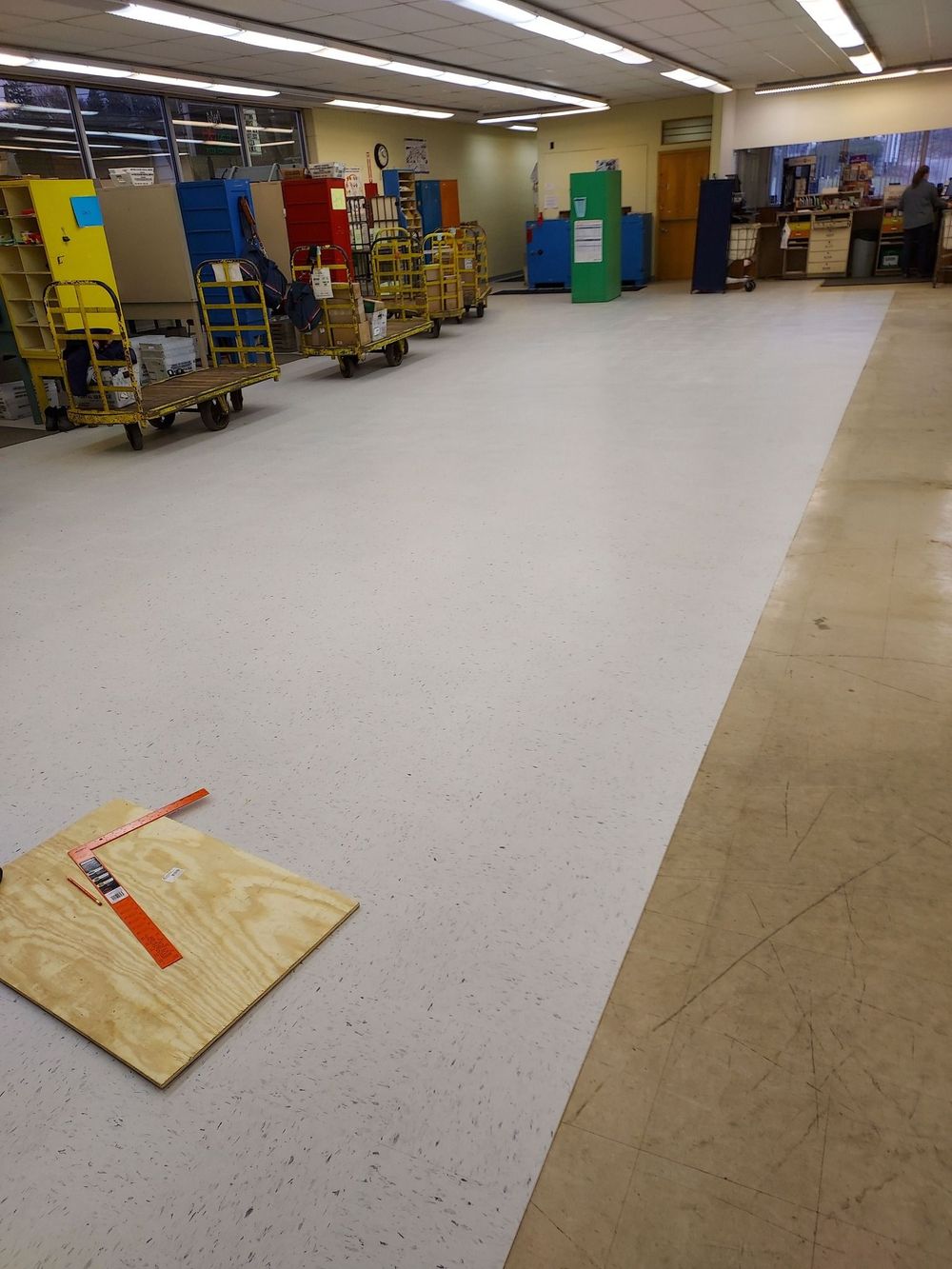 A brightly lit retail backroom with a freshly installed white speckled floor next to an older beige concrete floor.