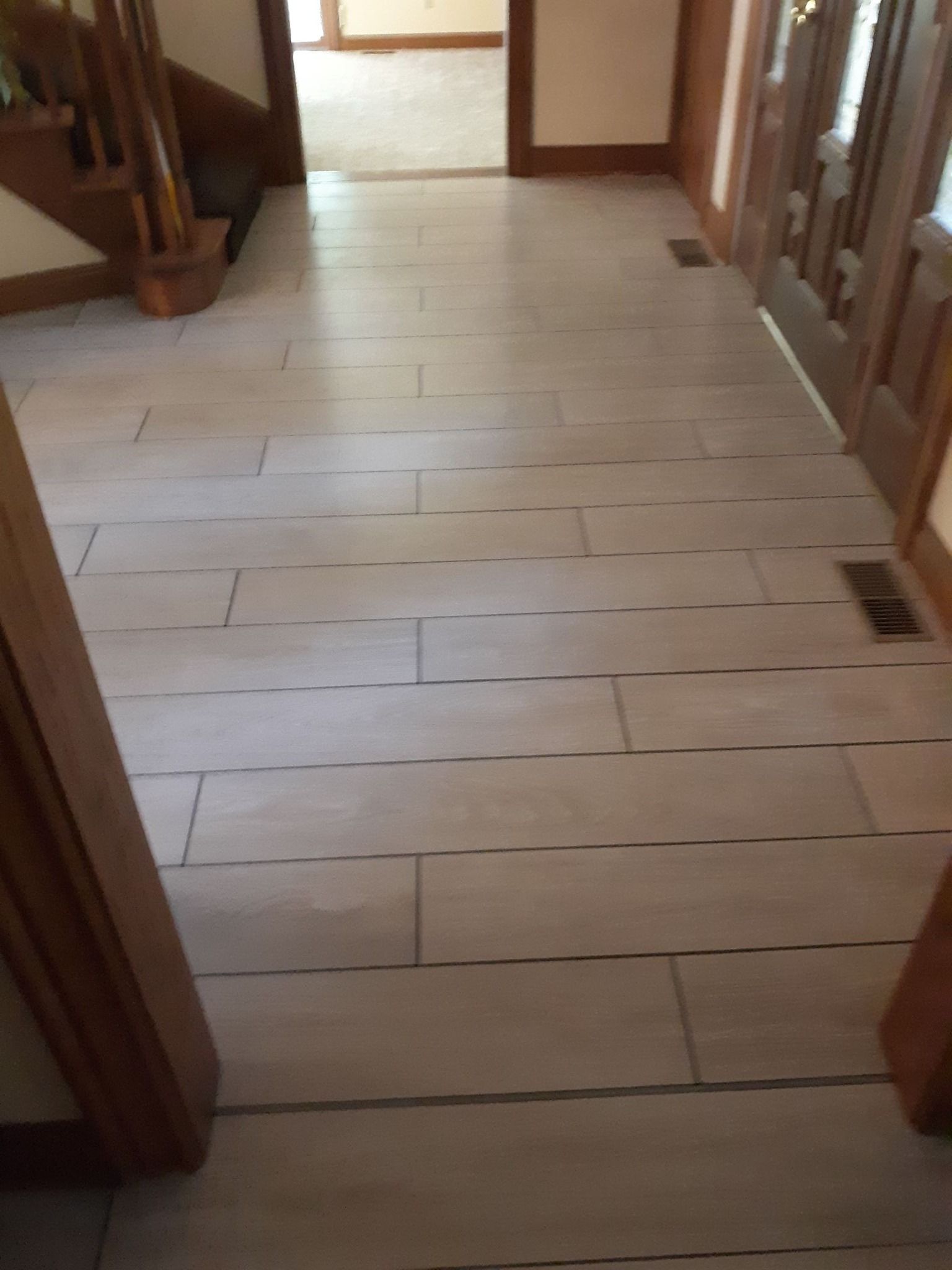 A hallway with light beige, rectangular floor tiles arranged in a brick pattern, viewed from the entryway.