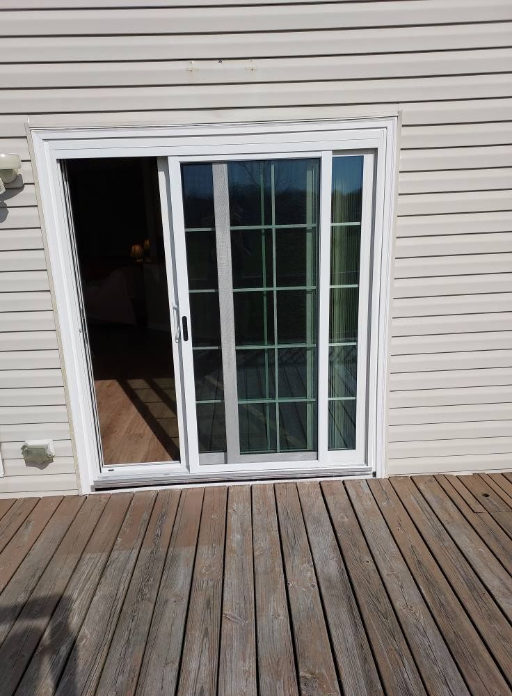A screened-in porch with white wooden railings and a wooden floor, opening to a yard with a parked white van.