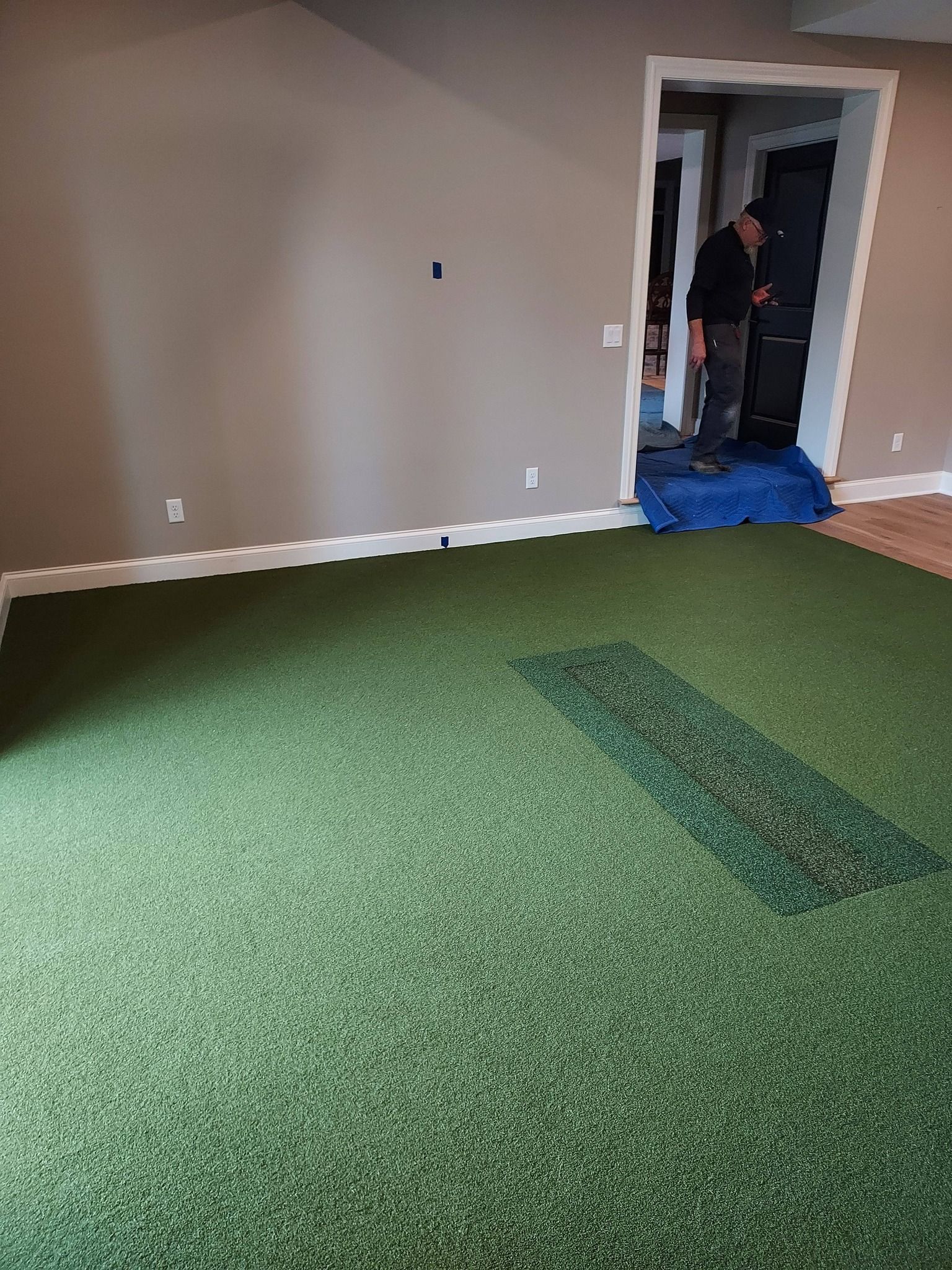 A person stands in a doorway behind a room with a newly installed artificial grass floor and a small turf inlay.