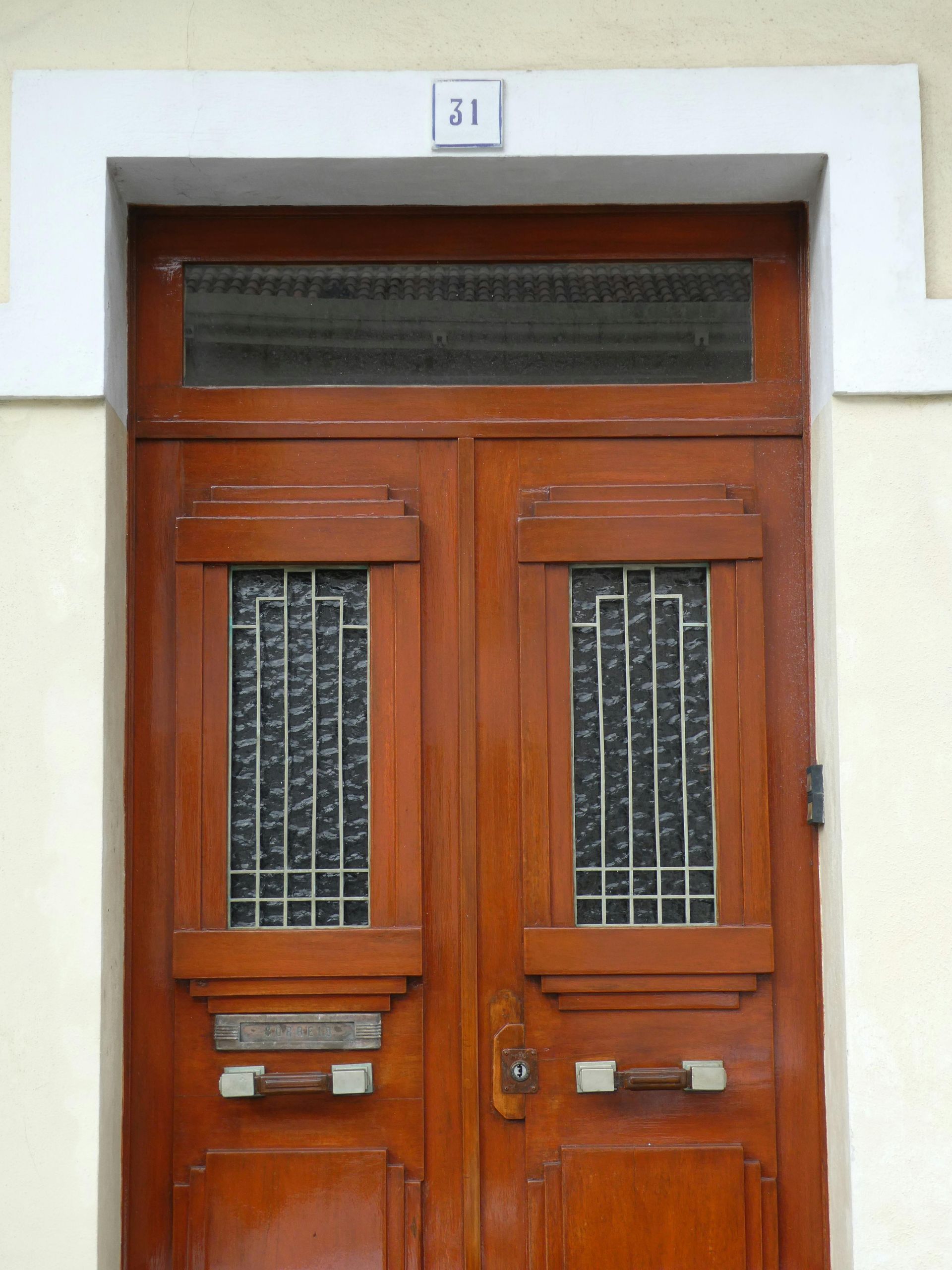 A partially open white sliding glass door with a grid pattern, installed on a house with beige siding and a wooden deck.