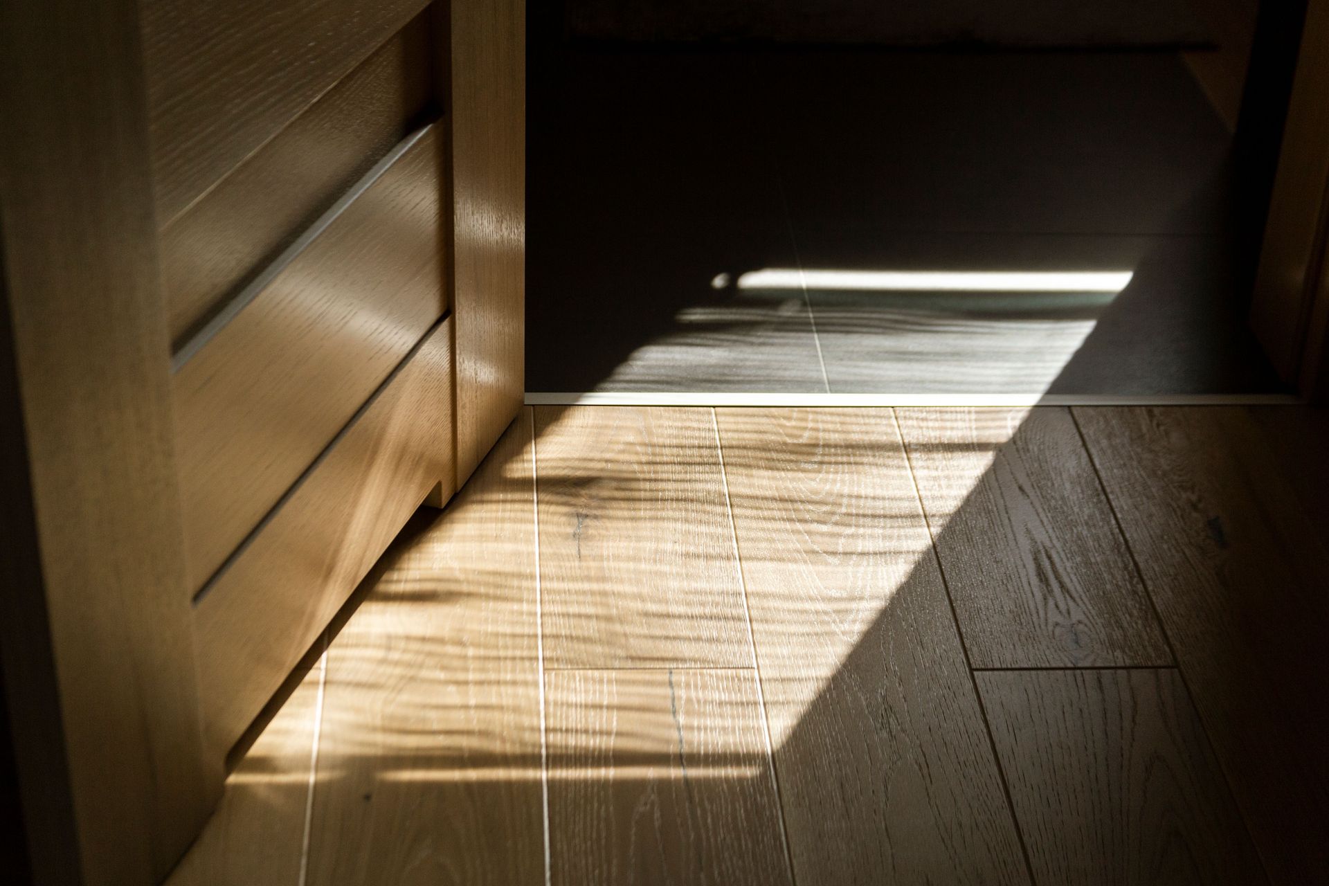 Sunlight streaming through blinds onto a wooden floor beside a cabinet