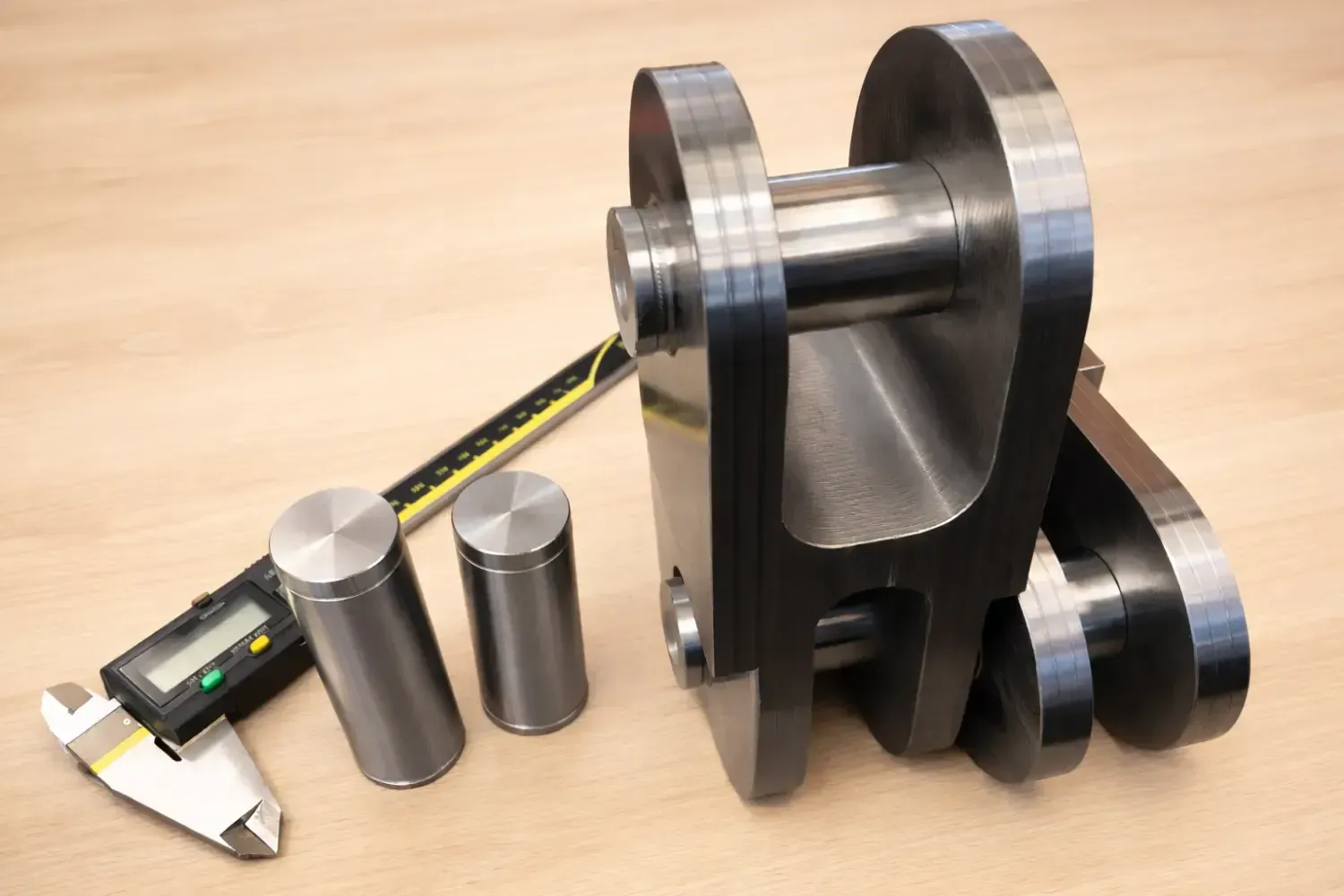Parti meccaniche in metallo e perni cilindrici accanto a calibri digitali su una superficie di legno.