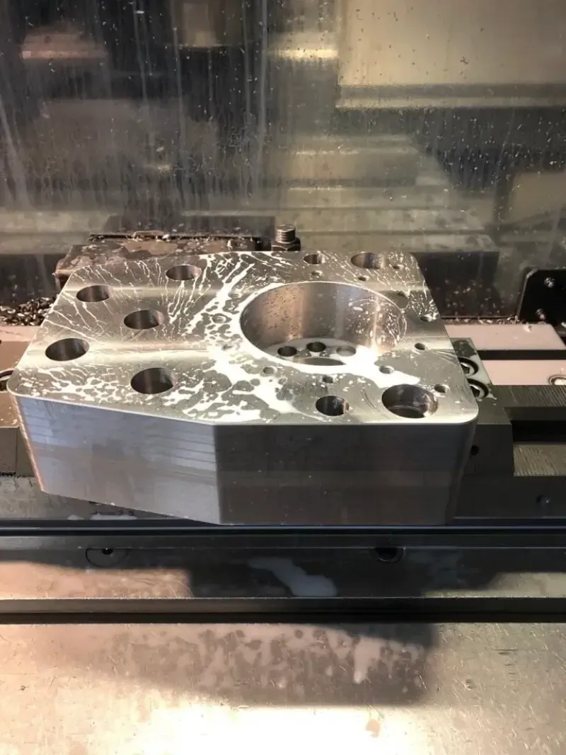 Un blocco di metallo lavorato da una macchina CNC, ricoperto di refrigerante e trucioli.