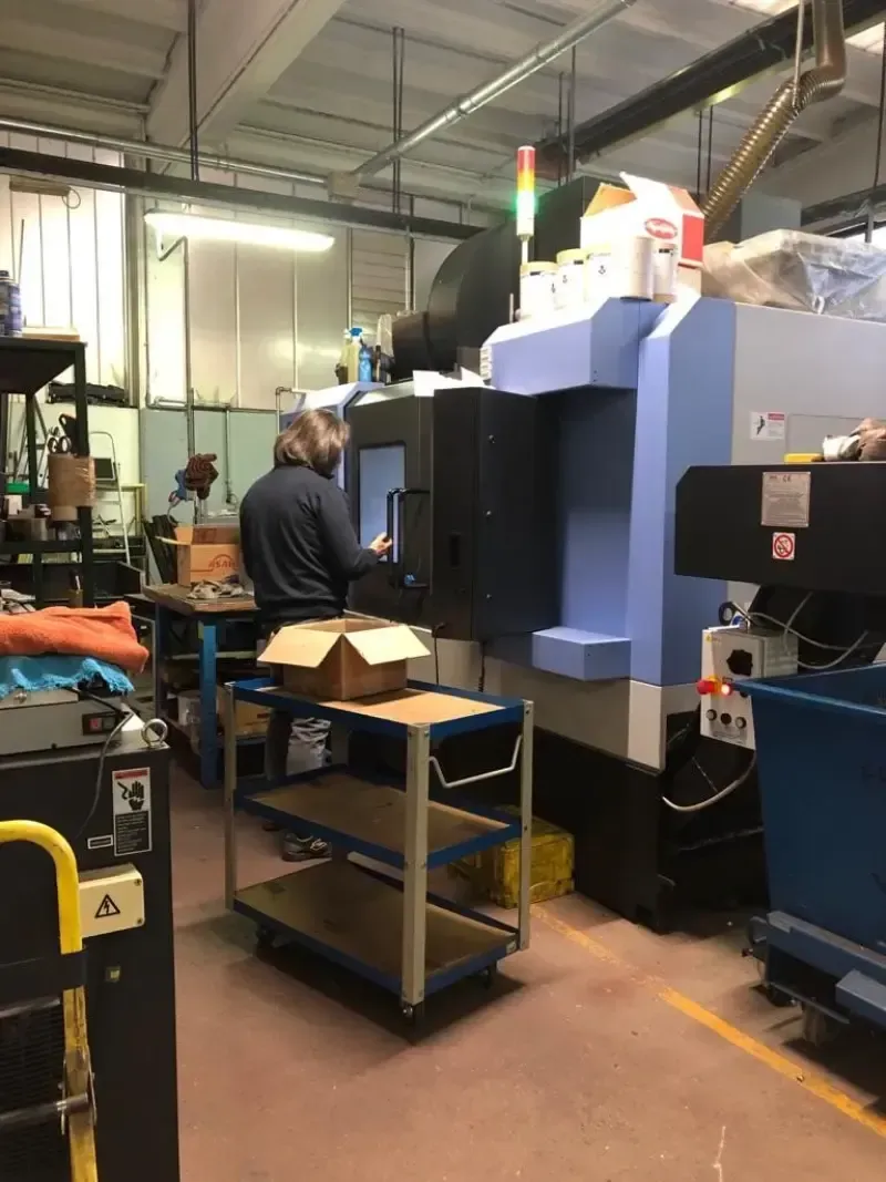 Persona che aziona una macchina CNC blu in un'officina. Davanti c'è un carrello con delle scatole.