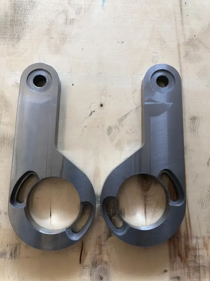 Due staffe metalliche grigie lavorate con intagli circolari e ad arco, appoggiate su una superficie di legno.