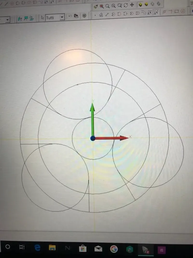 Un disegno CAD mostra cerchi concentrici, linee radianti e cerchi sovrapposti con assi.