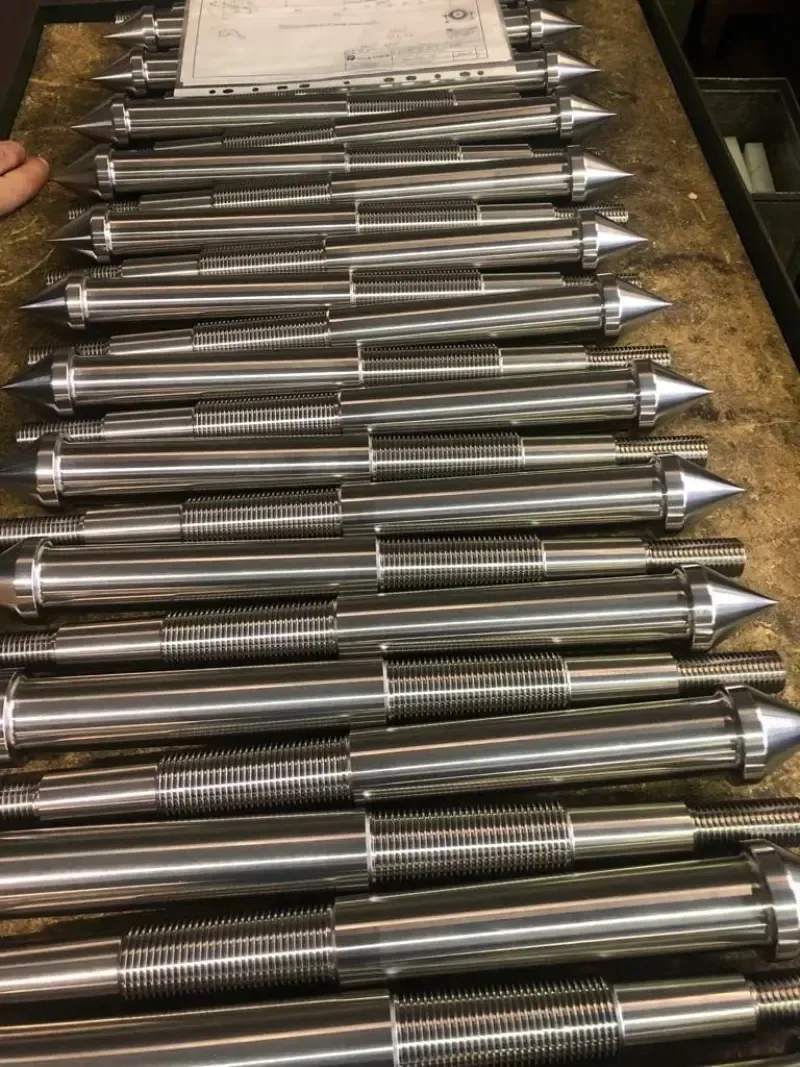 Barre di metallo lavorate e finite con estremità appuntite, disposte in file su una superficie di lavoro.