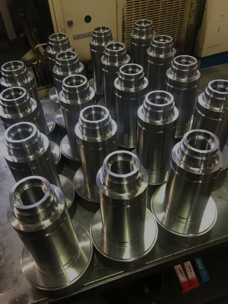 Diverse parti metalliche lavorate con forme cilindriche e flangiate, disposte su una superficie.