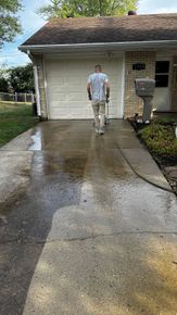 A man is cleaning the driveway of a house with a pressure washer.