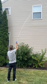 A man is washing the side of a house with a hose.