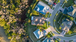 Aerial view of a suburban neighborhood with a straight street lined by houses and palm trees under a clear sky