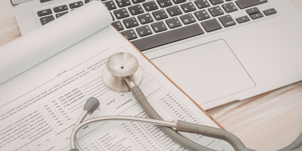 Stethoscope and medical paperwork on top of laptop. Healthcare concept.