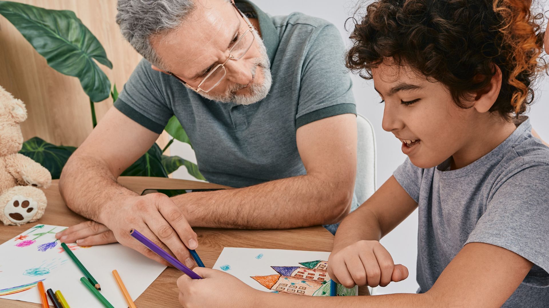 A man and a boy are sitting at a table drawing with markers.