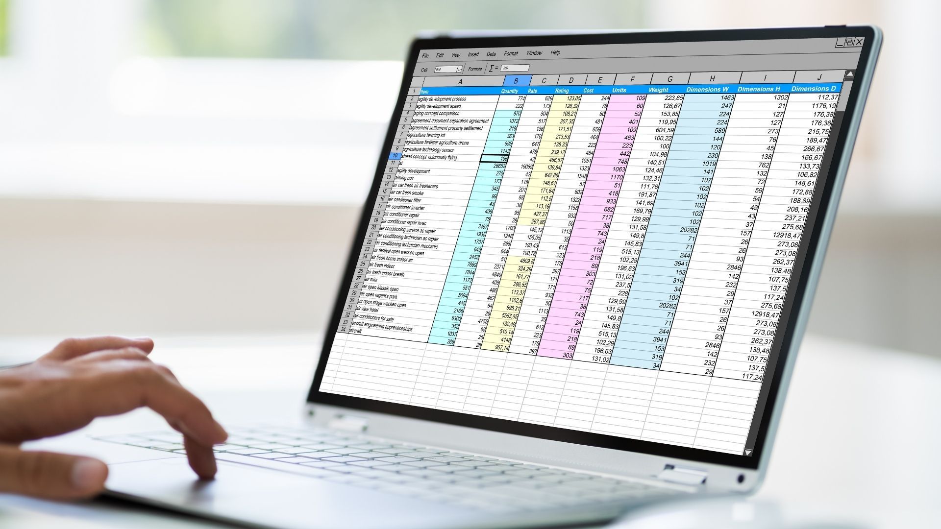 Hand on a laptop showing a colorful spreadsheet with multiple columns of data