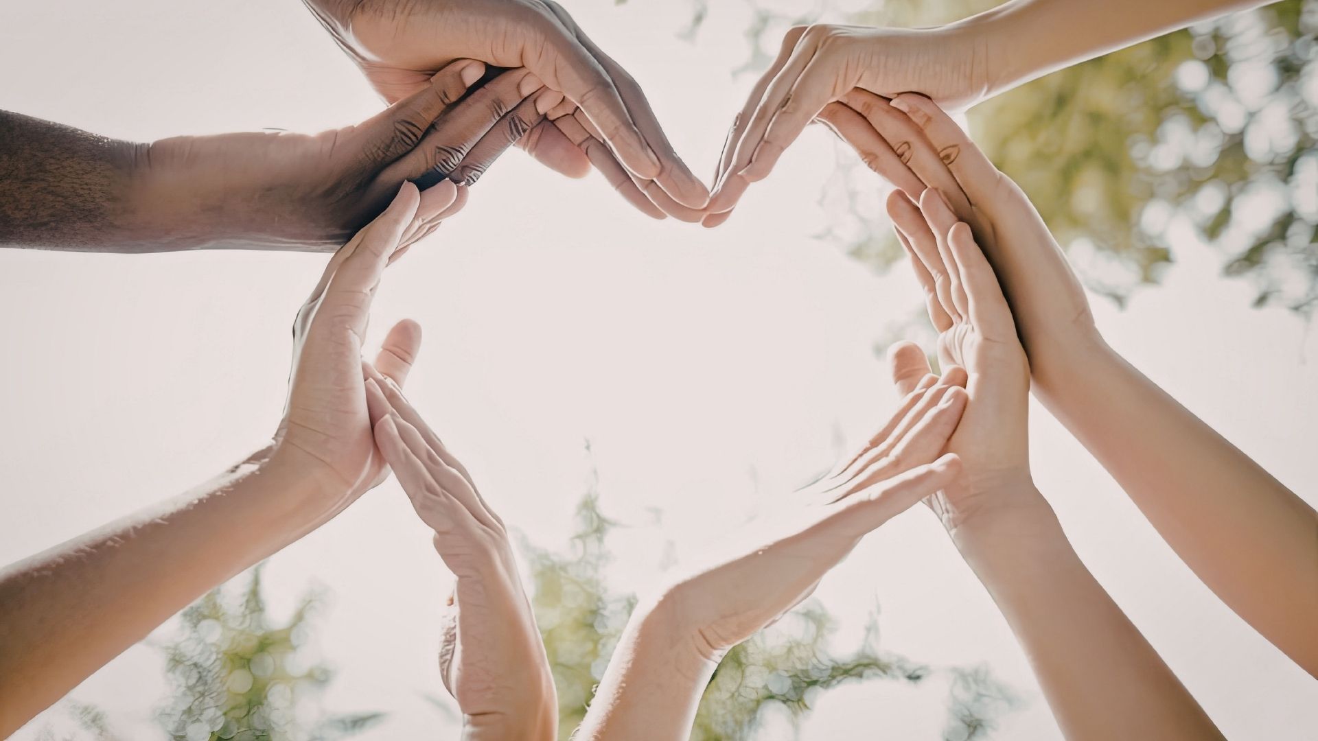 Hands forming a heart shape against a bright sky outdoors