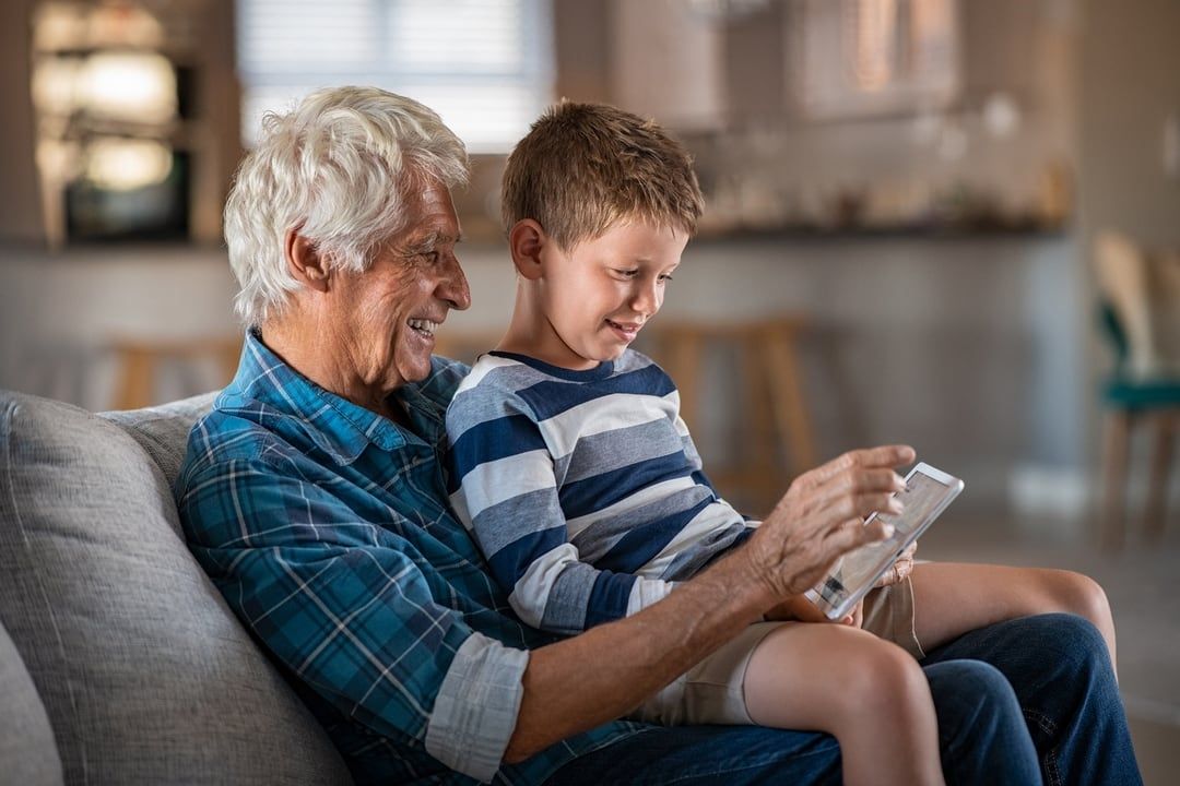 An elderly man and a young boy are sitting on a couch looking at a cell phone.