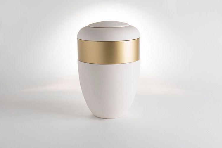A white vase with a gold stripe on the side is sitting on a white table.